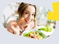 Uśmiechnięta kobieta je sałatkę z łososiem, zastanawiając się, ile omega 3 dziennie jest optymalne.