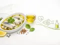 Śledzie w oleju, bogate w Omega-3, są zdrowe dla serca. Na talerzu śledzie z cebulą, cytryną i ziołami.