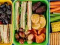 Kolorowe pojemniki pełne niskokaloryczne przekąski: kanapki, owoce, warzywa i ciastka. Idealne na zdrowy lunch.