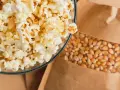 Misternie przygotowany popcorn w szklanej misce obok ziaren kukurydzy w papierowej torbie. Czy popcorn tuczy? Zależy od dodatków!