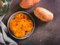 Chrupiące chipsy z batatów na talerzu, obok surowych bulw. Niska zawartość cukru sprawia, że bataty indeks glikemiczny mają korzystny wpływ na dietę.