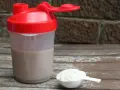 Shaker z napojem i miarka z proszkiem. To właśnie proteiny, klucz do regeneracji mięśni po treningu.