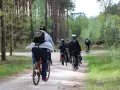 Grupa rowerzystów jedzie leśną ścieżką wśród drzew.