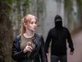 Kobieta z gazem pieprzowym w dłoni, w tle mężczyzna w kapturze.