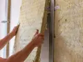 Montaż wełny mineralnej na ścianie, by zagłuszyć hałasy od uciążliwego sąsiada z góry.