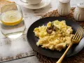 Puszysta jajecznica z truflami na czarnym talerzu, obok szklanka wody z cytryną i kromki chleba. Idealna na śniadanie, znasz jej jajecznica kcal?