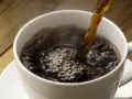 Gorąca kawa w białej filiżance, parująca i tworząca bąbelki. Czy kawa wpływa na cholesterol?