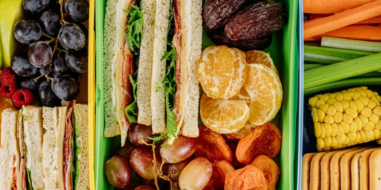 Kolorowe pojemniki pełne niskokaloryczne przekąski: kanapki, owoce, warzywa i ciastka. Idealne na zdrowy lunch.
