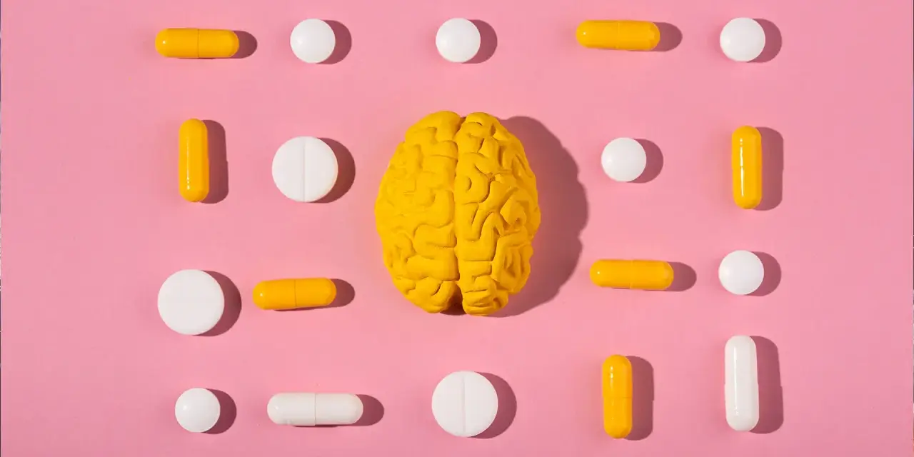 Żółty model mózgu otoczony białymi i żółtymi tabletkami i kapsułkami, symbolizującymi równowagę neuroprzekaźników, jak serotonina.