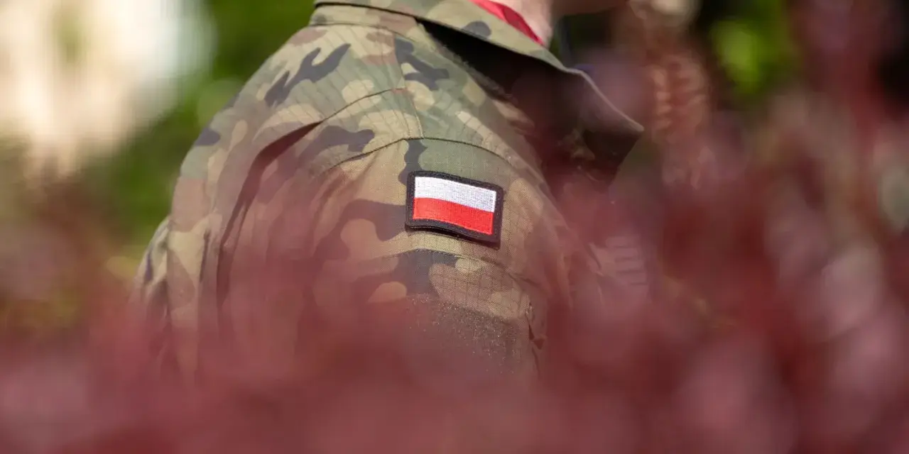 Żołnierz w mundurze z polską flagą. W tle zamazane czerwone liście i zieleń. Choroby dyskwalifikujące ze służby wojskowej mogą wpłynąć na możliwość noszenia takiego munduru.
