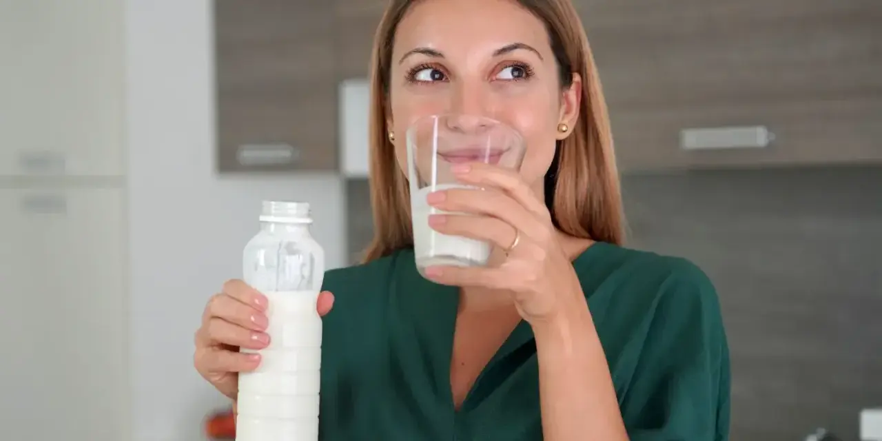 Kobieta pije kefir z butelki i szklanki. Idealny napój na noc dla zdrowia.