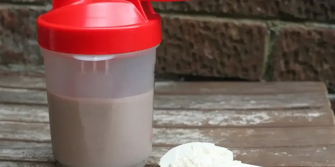 Shaker z napojem i miarka z proszkiem. To właśnie proteiny, klucz do regeneracji mięśni po treningu.
