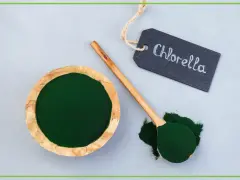 Chlorella w proszku w drewnianej miseczce i na łyżce. Tabliczka z napisem "Chlorella" podpowiada, jak stosować ten zielony proszek.