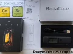 Zestaw Radiacode z dozymetrem ZERO, instrukcją i kablem USB. Obok pudełka z urządzeniem znajduje się karta z informacjami o izotopach Co-60 i Sr-90.