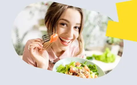 Uśmiechnięta kobieta je sałatkę z łososiem, zastanawiając się, ile omega 3 dziennie jest optymalne.