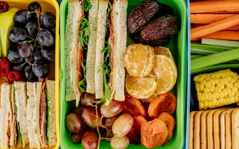 Kolorowe pojemniki pełne niskokaloryczne przekąski: kanapki, owoce, warzywa i ciastka. Idealne na zdrowy lunch.