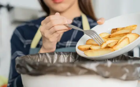 Kobieta wyrzuca frytki, zaczynając drogę do tego, jak obniżyć cholesterol bez leków. Zdrowa dieta to klucz.