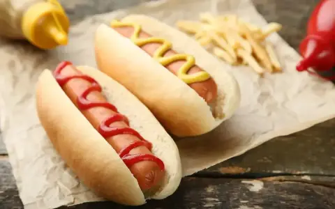 Dwa hot dogi, jeden z keczupem, drugi z musztardą, obok frytek. Zastanawiasz się, ile kalorii ma hot dog?