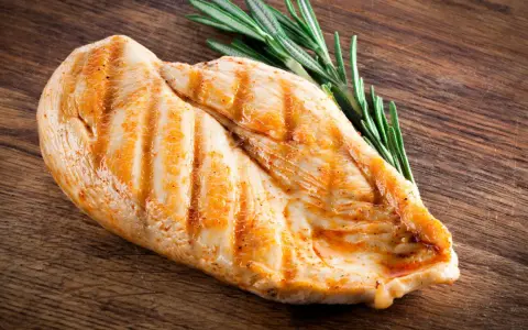 Grillowana pierś z kurczaka z rozmarynem na drewnianej desce. Zastanawiasz się, ile białka ma pierś z kurczaka? To świetne źródło!