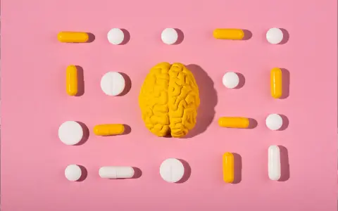 Żółty model mózgu otoczony białymi i żółtymi tabletkami i kapsułkami, symbolizującymi równowagę neuroprzekaźników, jak serotonina.