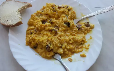 Jajecznica z grzybami na talerzu, obok kromka chleba z masłem. Ile jajek dziennie? To zależy od apetytu!