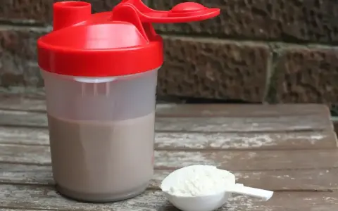 Shaker z napojem i miarka z proszkiem. To właśnie proteiny, klucz do regeneracji mięśni po treningu.