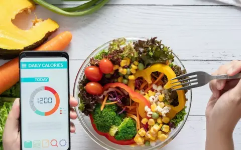 Aplikacja pokazuje 1200 kcal, podczas gdy ręka sięga widelcem po świeżą sałatkę.