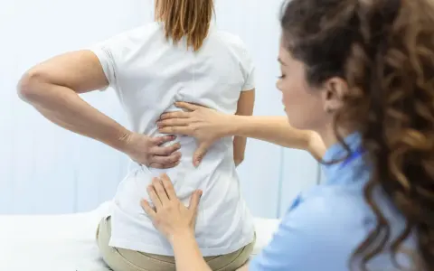 Fizjoterapeuta bada plecy pacjentki. Po długiej rehabilitacji wreszcie wyleczyłem kręgozmyk i czuję się znacznie lepiej.