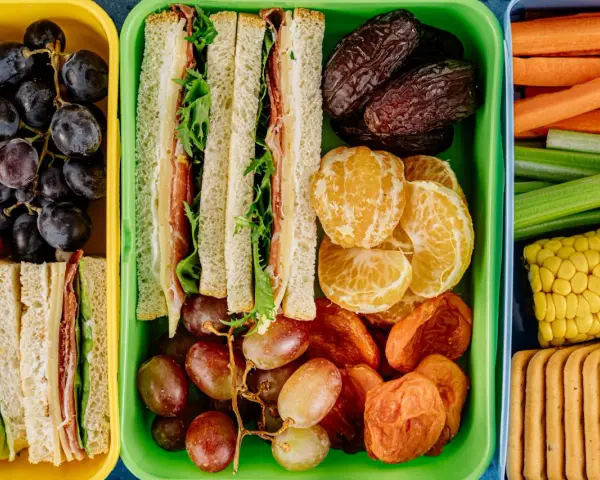 Kolorowe pojemniki pełne niskokaloryczne przekąski: kanapki, owoce, warzywa i ciastka. Idealne na zdrowy lunch.