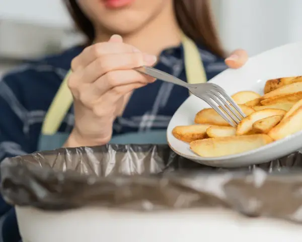 Kobieta wyrzuca frytki, zaczynając drogę do tego, jak obniżyć cholesterol bez leków. Zdrowa dieta to klucz.