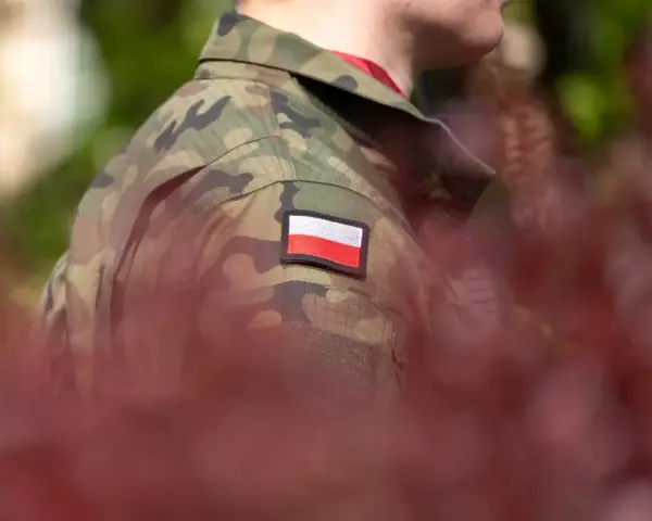 Żołnierz w mundurze z polską flagą. W tle zamazane czerwone liście i zieleń. Choroby dyskwalifikujące ze służby wojskowej mogą wpłynąć na możliwość noszenia takiego munduru.