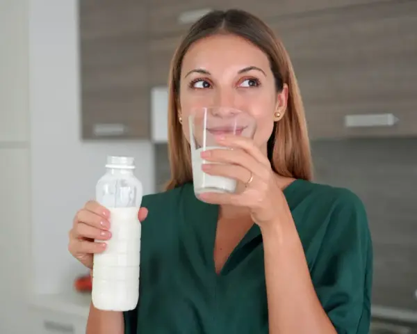 Kobieta pije kefir z butelki i szklanki. Idealny napój na noc dla zdrowia.