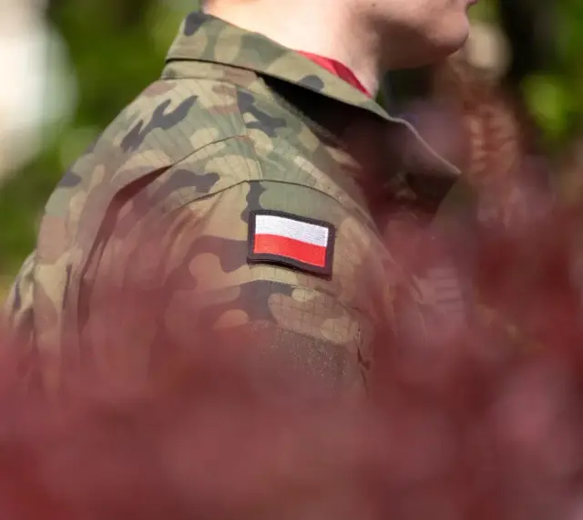 Żołnierz w mundurze z polską flagą. W tle zamazane czerwone liście i zieleń. Choroby dyskwalifikujące ze służby wojskowej mogą wpłynąć na możliwość noszenia takiego munduru.