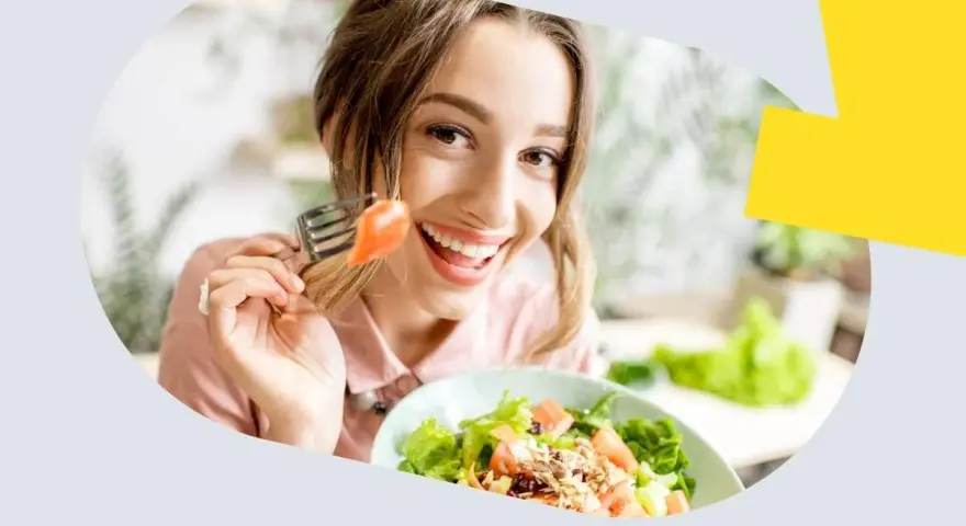 Uśmiechnięta kobieta je sałatkę z łososiem, zastanawiając się, ile omega 3 dziennie jest optymalne.