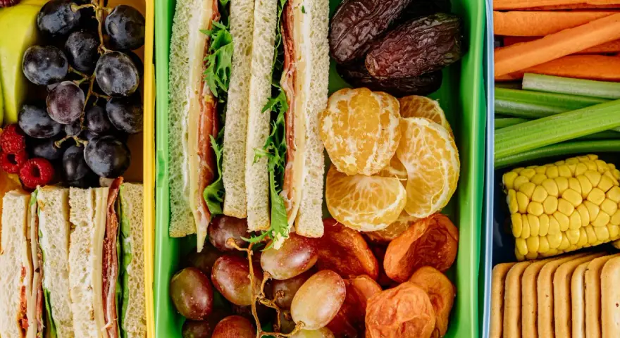 Kolorowe pojemniki pełne niskokaloryczne przekąski: kanapki, owoce, warzywa i ciastka. Idealne na zdrowy lunch.