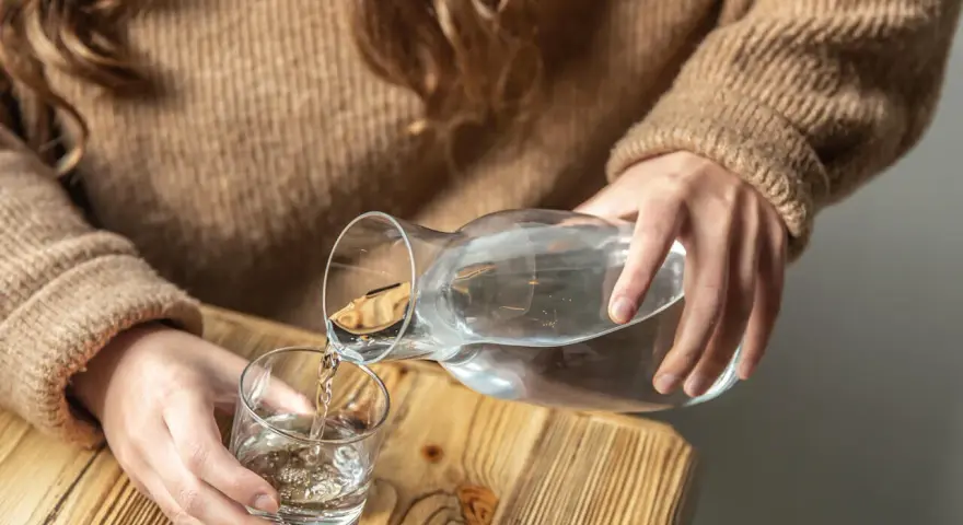 Dłonie nalewają wodę z karafki do szklanki. Pamiętaj, by stay hydrated.