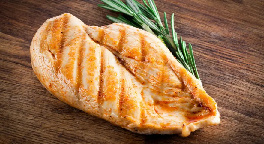 Grillowana pierś z kurczaka z rozmarynem na drewnianej desce. Zastanawiasz się, ile białka ma pierś z kurczaka? To świetne źródło!