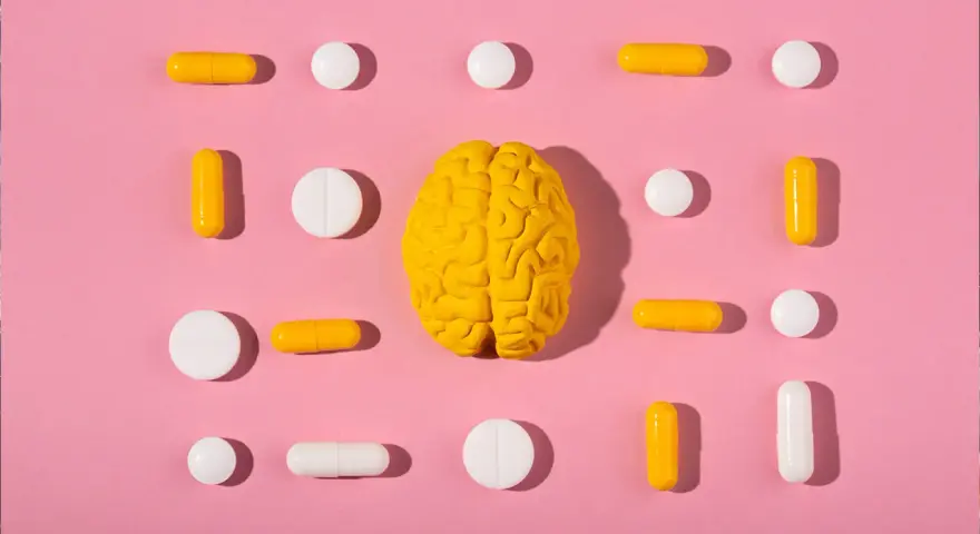 Żółty model mózgu otoczony białymi i żółtymi tabletkami i kapsułkami, symbolizującymi równowagę neuroprzekaźników, jak serotonina.