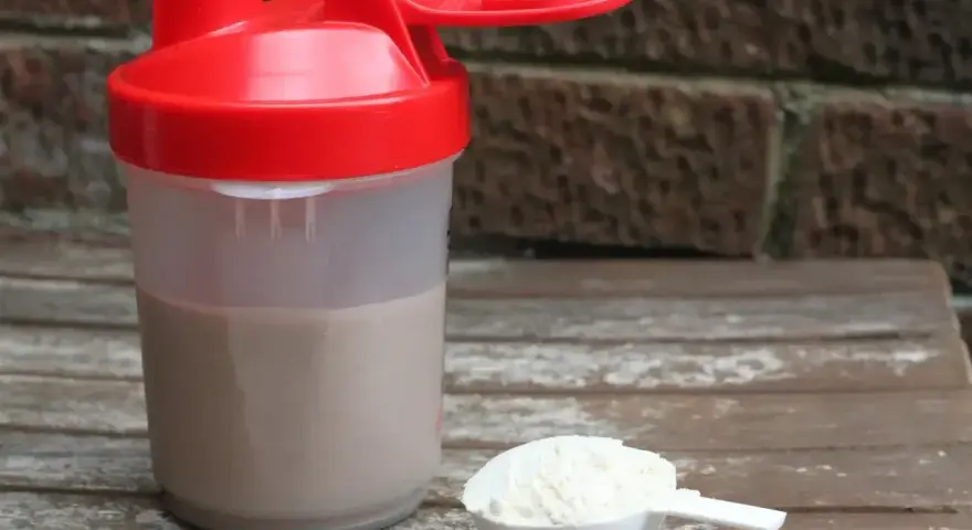 Shaker z napojem i miarka z proszkiem. To właśnie proteiny, klucz do regeneracji mięśni po treningu.