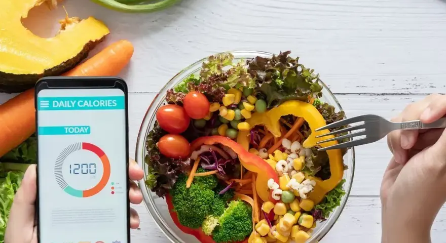Aplikacja pokazuje 1200 kcal, podczas gdy ręka sięga widelcem po świeżą sałatkę.