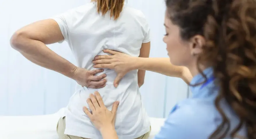Fizjoterapeuta bada plecy pacjentki. Po długiej rehabilitacji wreszcie wyleczyłem kręgozmyk i czuję się znacznie lepiej.