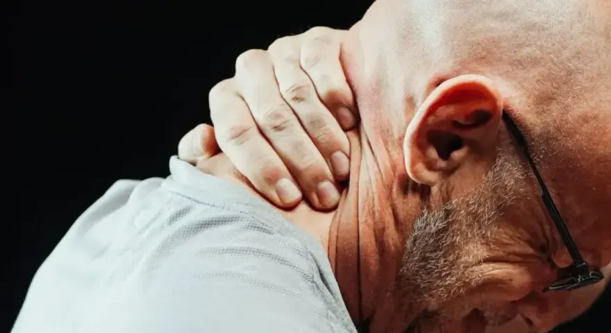 Mężczyzna z bólem szyi przy skręcaniu głowy, trzymający się za kark.