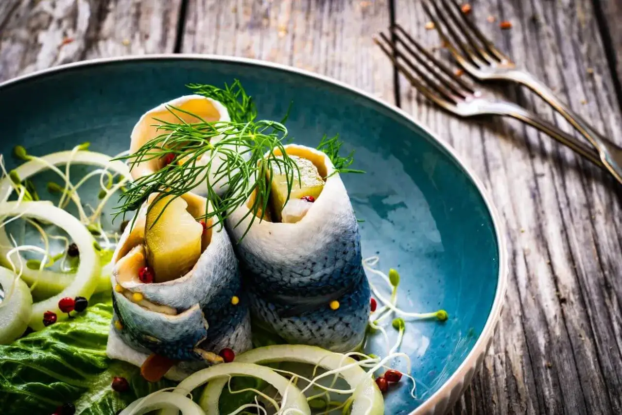 Roladki ze śledzia w oleju z ogórkiem i koperkiem, podane z cebulą. Czy śledzie w oleju są zdrowe? Tak, to bogactwo kwasów omega-3!