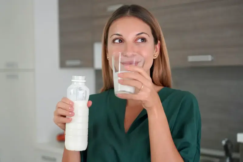 Kobieta pije kefir z butelki i szklanki. Idealny napój na noc dla zdrowia.
